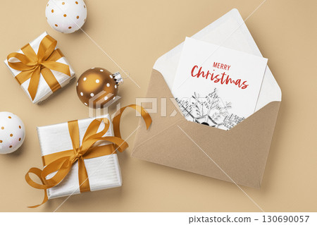 Christmas holiday card in envelope with present gift boxes with gold bow ribbon and xmas ball ornament on brown background Christmas holiday card in envelope with present gift boxes with gold bow ribbon and xmas ball ornament on brown background 130690057
