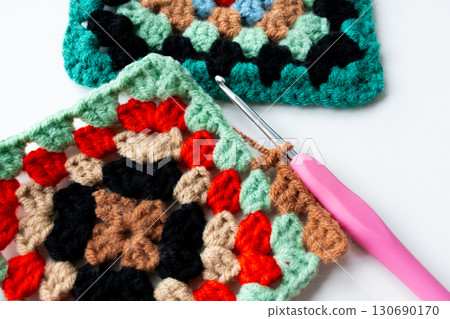 Colorful crochet granny squares with pink hook on white background 130690170