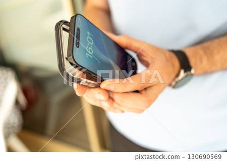 Close-up of a man holding a smartphone and a transparent protective case, preparing to put the case on the phone. 130690569