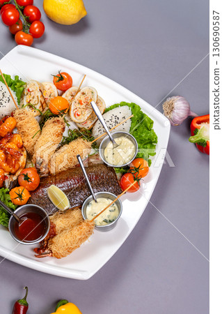 Grilled fish, spicy shrimp, spring rolls, and rice on a white plate. Top view on gray background Grilled fish, spicy shrimp, spring rolls, and rice on a white plate. Top view on gray background 130690587