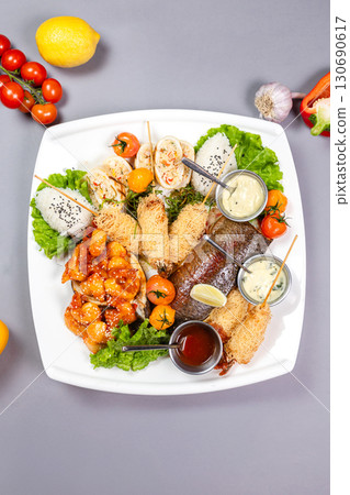 Grilled fish, spicy shrimp, spring rolls, and rice on a white plate. Top view on gray background 130690617