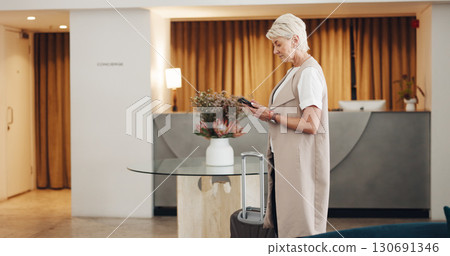 Woman, hotel and reception lobby with smartphone, connection and business trip with email, suitcase and typing. Senior person, employee and travel agent with a cellphone, social media and hallway 130691346