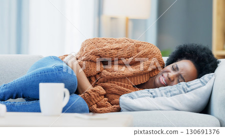 Stomach pain, pms and black woman on a sofa with anxiety, gas or endometriosis at home. Menstruation, constipation and African female with period crisis, stress or digestion problem in a living room 130691376