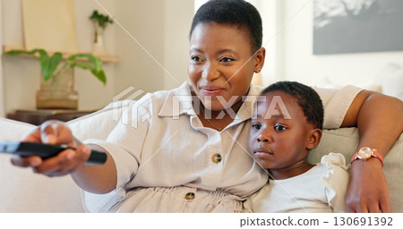 Watching tv, child and mom with remote in home to relax with streaming movies, show or series on weekend. Living room, sofa and happy black family with a film online in lounge with love and hug Watching tv, child and mom with remote in home to relax with streaming movies, show or series on weekend. Living room, sofa and happy black family with a film online in lounge with love and hug 130691392