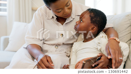 Mother, child and phone on sofa, watching and learning educational show for development, technology and understanding. Serious, conversation and bonding with embrace, couch and reading text message 130691442
