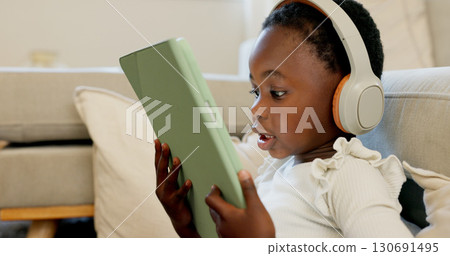 Black child, tablet and headphones for home education, language e learning and translation or video streaming. Kid or girl listening to audio and watch on digital technology for games and school Black child, tablet and headphones for home education, language e learning and translation or video streaming. Kid or girl listening to audio and watch on digital technology for games and school 130691495