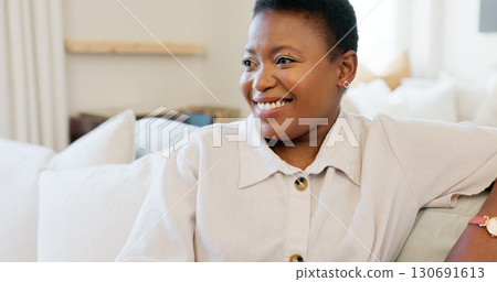Happy, smile and a black woman on a sofa to relax while watching tv in the living room of a house. Home, laughing and an African lady streaming a movie while sitting on a couch in her lounge 130691613