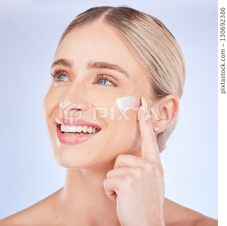 Face, beauty skincare and woman with cream in studio isolated on a blue background. Dermatology cosmetics, thinking and happy female model apply lotion, creme or moisturizer product for healthy skin. 130692386