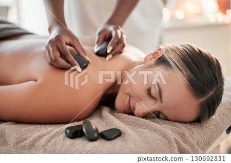 Woman, hot stone massage and therapist, hands and zen with holistic therapy and spa treatment for back. Calm, peace of mind and face, healing and stress relief with self care at wellness resort 130692831