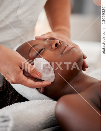 Black woman face, relax and gua sha stone spa treatment of a young female with facial. Skincare, beauty and wellness clinic with client feeling calm and zen from massage and dermatology glow Black woman face, relax and gua sha stone spa treatment of a young female with facial. Skincare, beauty and wellness clinic with client feeling calm and zen from massage and dermatology glow 130693264