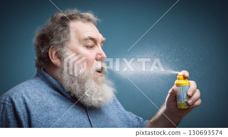 Bearded man spraying throat medicine for relief in indoor setting 130693574