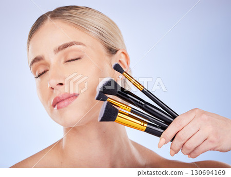 Eyes closed, face and makeup of woman with brushes in studio isolated on a blue background. Facial cosmetics, beauty skincare and female model with tools to apply foundation or powder for aesthetics. Eyes closed, face and makeup of woman with brushes in studio isolated on a blue background. Facial cosmetics, beauty skincare and female model with tools to apply foundation or powder for aesthetics. 130694169