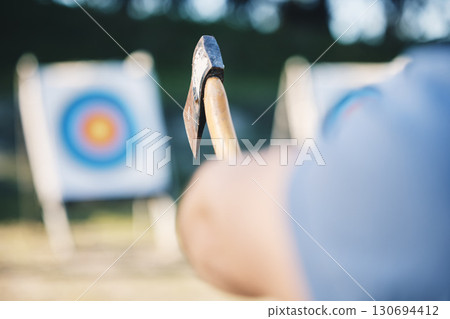 Man throwing axe at sports range, archery training or practice with board circle for goal, game and exercise. Strong person closeup with weapon for tomahawk competition, gaming park and eye target 130694412