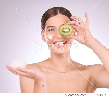 Woman, face and kiwi with moisturizer for skincare nutrition, cream or healthy diet against gray studio background. Portrait of happy female with fruit and creme for natural organic facial cosmetics Woman, face and kiwi with moisturizer for skincare nutrition, cream or healthy diet against gray studio background. Portrait of happy female with fruit and creme for natural organic facial cosmetics 130694894