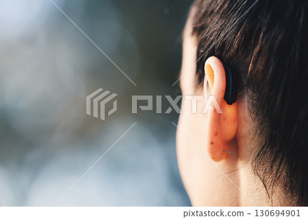 Woman, ear and hearing aid implant for disability with free space for mockup or advertising. Deaf person with medical device for listening to sound or audio with technology for wellness outdoor 130694901