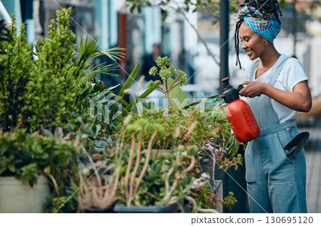 Water, flowers or black woman gardening in small business shop for healthy leaf or organic plants growth. Irrigation, store manager or girl entrepreneur watering floral agriculture with a happy smile 130695120
