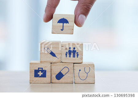 Hands, wood and building blocks on table for insurance, healthcare or a safe healthy foundation. Hand of doctor putting small wooden block, object or icons with umbrella to build medical investment Hands, wood and building blocks on table for insurance, healthcare or a safe healthy foundation. Hand of doctor putting small wooden block, object or icons with umbrella to build medical investment 130695398