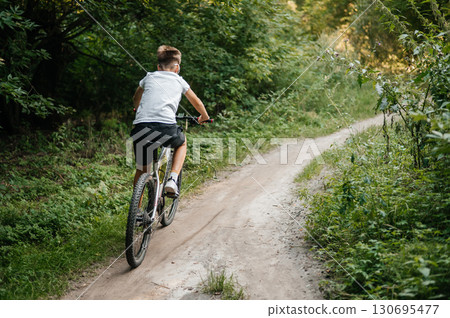 Teenager riding bicycle along forest trail on sunny day. Outdoor activity, adventure and healthy lifestyle concep 130695477