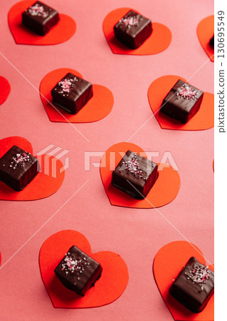 Dark chocolate candy on red paper hearts, flat lay on pink background, Valentine concept Dark chocolate candy on red paper hearts, flat lay on pink background, Valentine concept 130695549