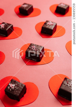 Dark chocolate candy on red paper hearts, flat lay on pink background, Valentine concept 130695559