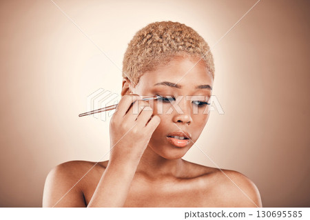 Black woman, beauty and brush for eye makeup on a brown background with cosmetics for face. Aesthetic model person in studio for transformation, self care and facial glow or shine on skin and eyes 130695585