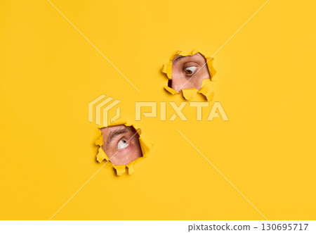 Human eyes peeking through yellow paper to each other 130695717