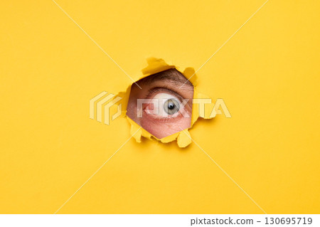 Human eye looking through torn yellow paper 130695719