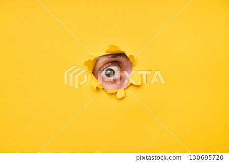 Human eye looking through torn yellow paper 130695720