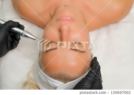 Close-up of a woman undergoing microneedling facial treatment in a beauty clinic, a professional skincare procedure aimed at rejuvenation, anti-aging, and improving skin texture. RF lifting. Close-up of a woman undergoing microneedling facial treatment in a beauty clinic, a professional skincare procedure aimed at rejuvenation, anti-aging, and improving skin texture. RF lifting. 130697002