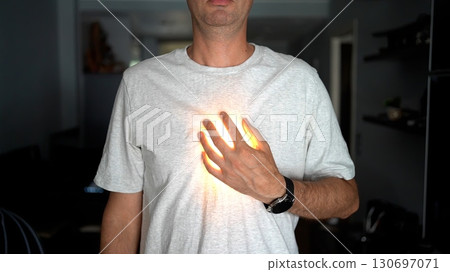A man in a white t-shirt places his hand on his chest with a glowing light effect under his hand, symbolizing heart, energy, or inner power. 130697071