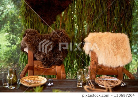 Two thrones for the wedding couple, in the Viking style. Heavy wooden tables and chairs decorated with animal skins and greenery. Massive composition Two thrones for the wedding couple, in the Viking style. Heavy wooden tables and chairs decorated with animal skins and greenery. Massive composition 130697204