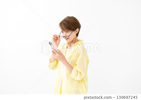 A woman looking at her smartphone with reading glasses 130697245