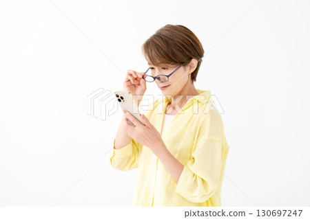 A woman looking at her smartphone with reading glasses 130697247