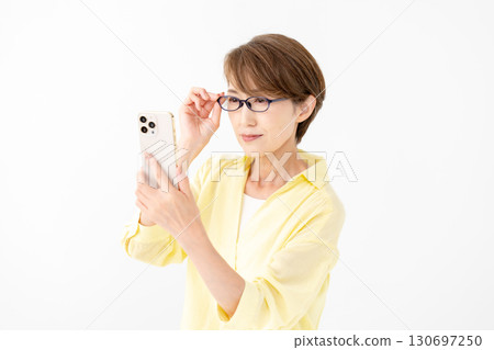 A woman looking at her smartphone with reading glasses A woman looking at her smartphone with reading glasses 130697250