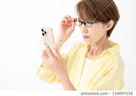 一位女士戴著老花眼鏡看著她的智慧型手機 130697256