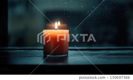 a lit orange candle in a dark window 130697366