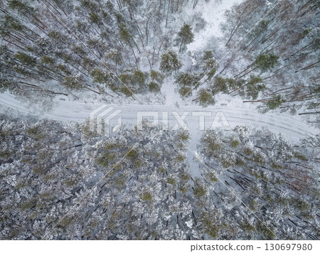 Aerial view of the road in the winter forest with high pine or spruce trees covered by snow. Driving in winter. 130697980