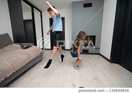 Two siblings engaging in an energetic indoor dance session on wooden floor in a modern living room during afternoon sunlight streaming through large windows Two siblings engaging in an energetic indoor dance session on wooden floor in a modern living room during afternoon sunlight streaming through large windows 130699608
