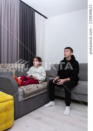 Siblings engaged in a thrilling video game session in a cozy living room during a winter evening at home, focusing on teamwork and friendly competition Siblings engaged in a thrilling video game session in a cozy living room during a winter evening at home, focusing on teamwork and friendly competition 130699621