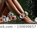 Women's feet with drops of water surrounded by flowers. The concept of foot massager, skin care and spa treatments. 130699657