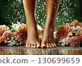 Women's feet with drops of water surrounded by flowers. The concept of foot massager, skin care and spa treatments. 130699659