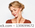 sad young woman holds sore cheek on white isolated background. Severe ache toothache. Problems and pain in teeth and gums. Dentistry and dental clinic 130699672