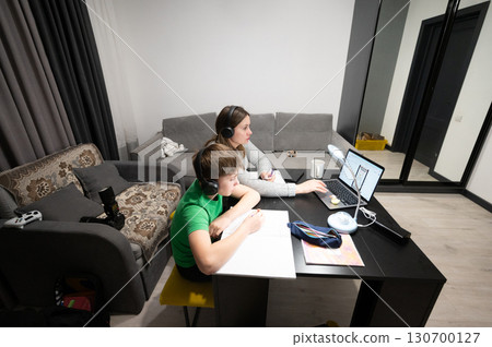 Engaging in virtual learning, a mother and her son explore lessons at home in a cozy, modern living room during the afternoon hours 130700127