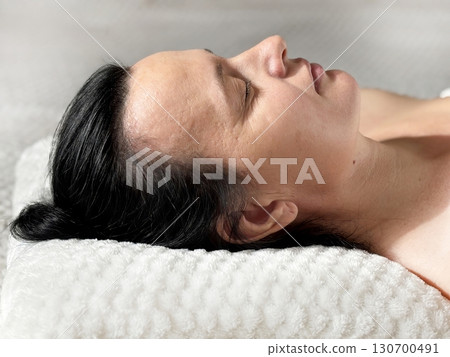 Brunette middle aged woman sleeping on white pillow and cosmetology couch during procedure in sunlight, top view. Concept of cosmetology, beauty treatment, relaxation, recovery and healthy sleep Brunette middle aged woman sleeping on white pillow and cosmetology couch during procedure in sunlight, top view. Concept of cosmetology, beauty treatment, relaxation, recovery and healthy sleep 130700491