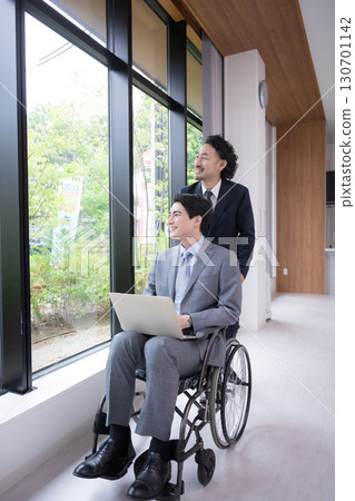 Business scene of two men in suits working in wheelchairs in the office, vertical Business scene of two men in suits working in wheelchairs in the office, vertical 130701142