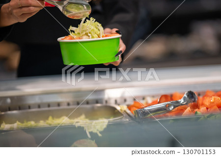 A close-up of a woman's hands with long red nails using metal tongs to serve food at a Weight-Pay cafeteria 130701153