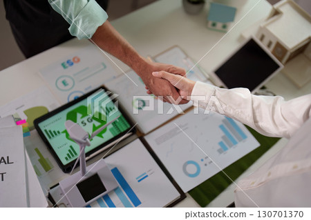 Top view of professionals shaking hands over ESG reports in a modern office. Top view of professionals shaking hands over ESG reports in a modern office. 130701370