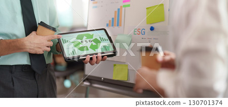 Businessman presenting ESG data on tablet while discussing with a colleague. 130701374