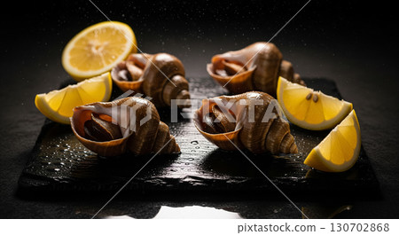 Fresh Whelks with Lemon Wedges on Slate Board 130702868