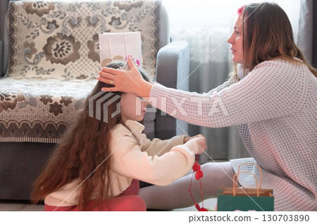 A mother gently places a crown on her daughter's head, a tender moment of shared joy and love. 130703890